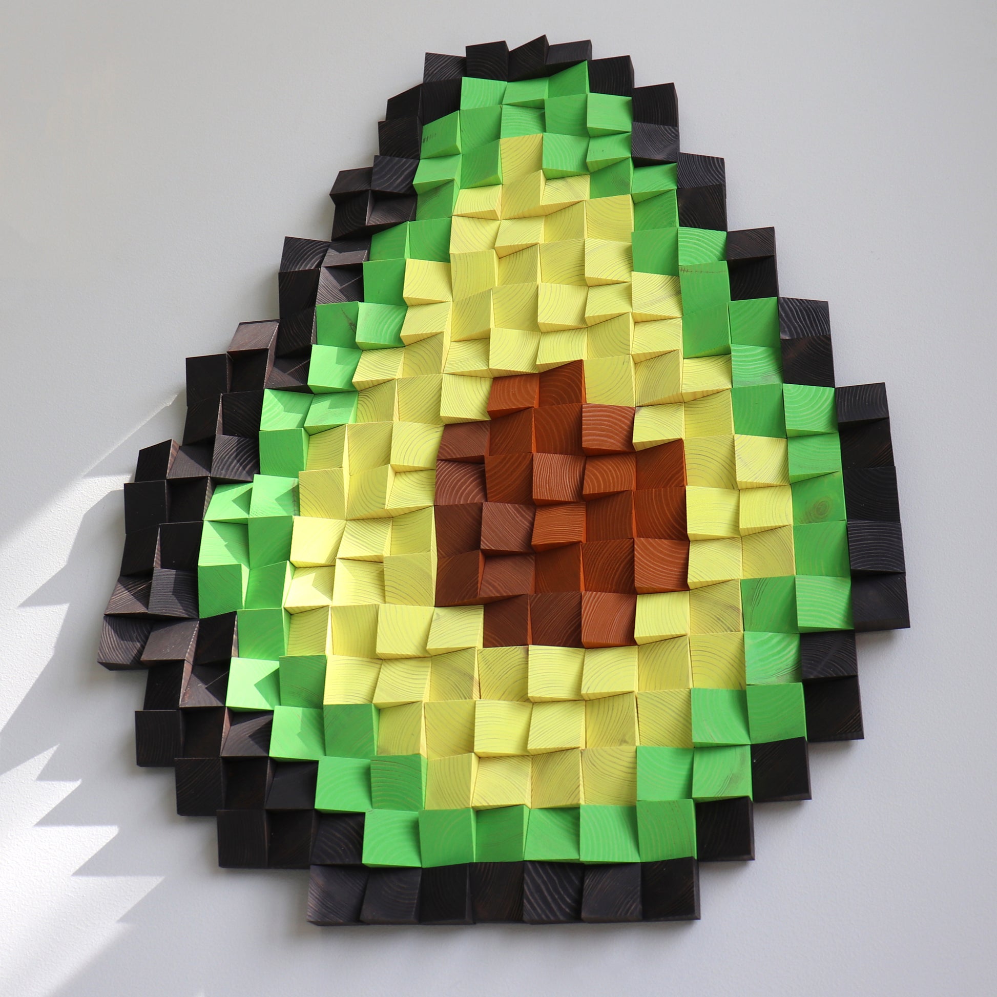 Wooden wall art shaped like an avocado slice, blending multiple green tones with a textured pit.