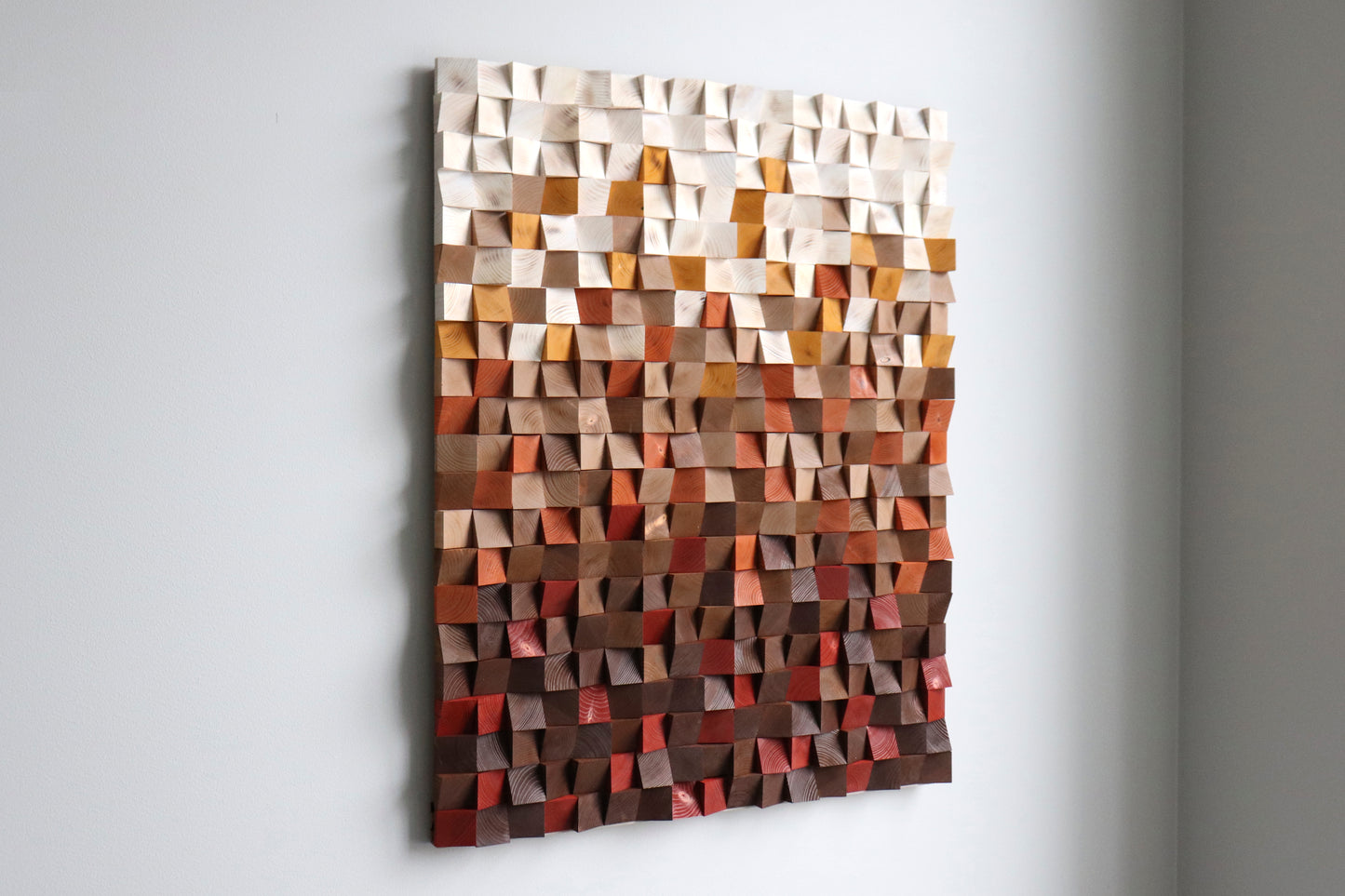 Left-angle view of handcrafted geometric wood wall panel with warm earth-tone gradient and 3D texture.