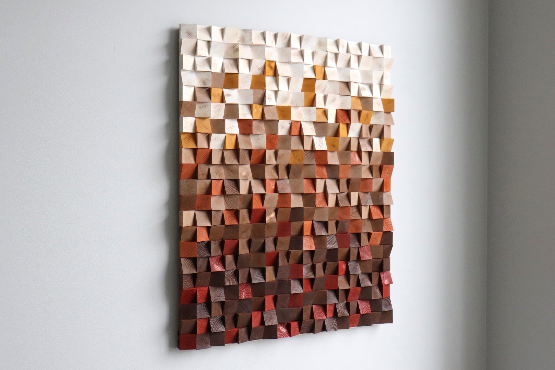 Left-angle view of handcrafted geometric wood wall panel with warm earth-tone gradient and 3D texture.